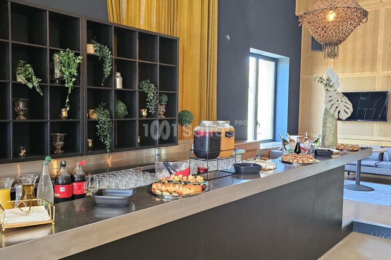 Buffet avec boissons, verrines et snacks disposés sur un comptoir moderne, décoré de plantes et éclairé naturellement.