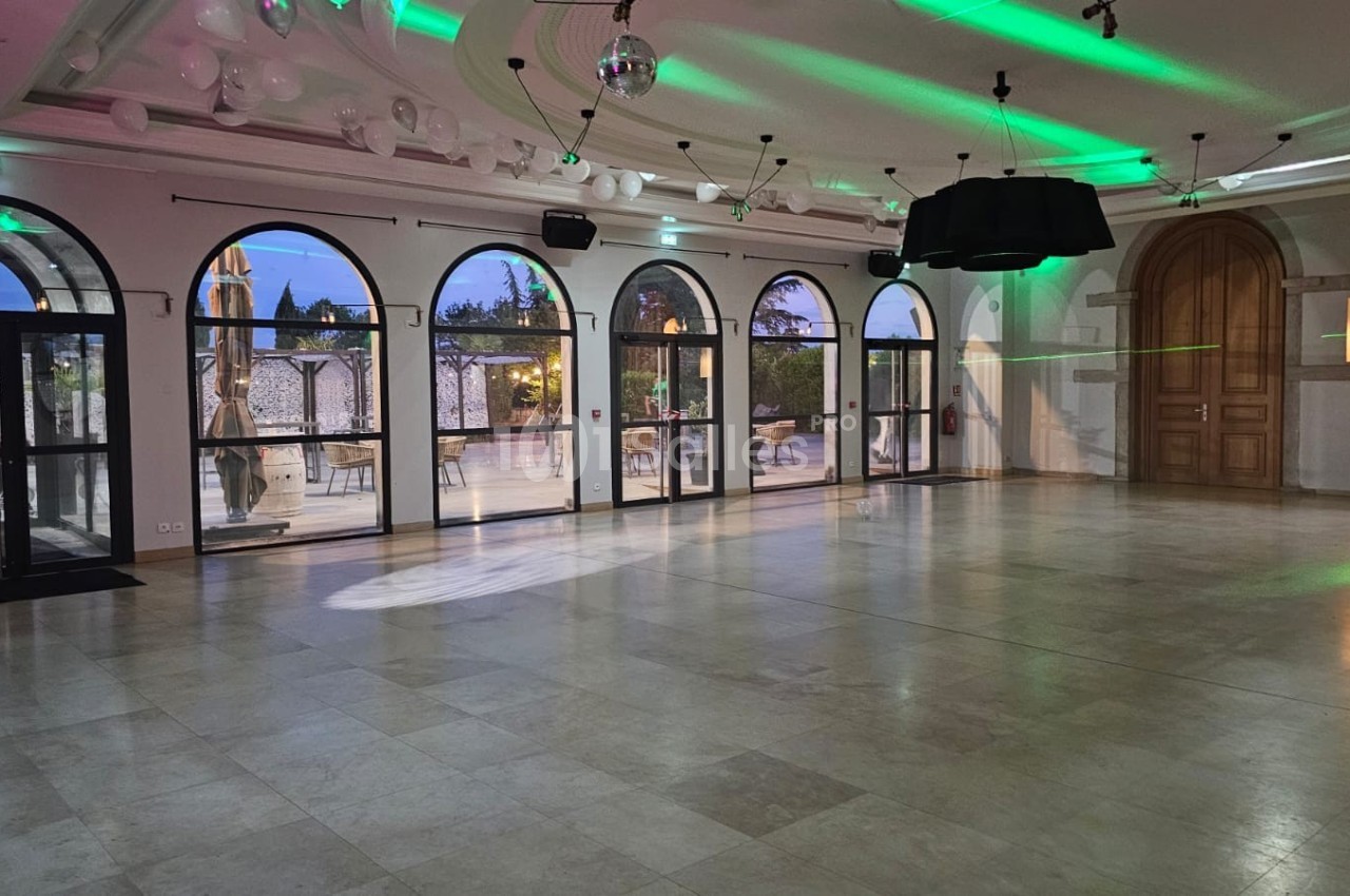 Salle spacieuse avec sol en marbre, grandes fenêtres cintrées et éclairage vert, donnant sur une terrasse extérieure.