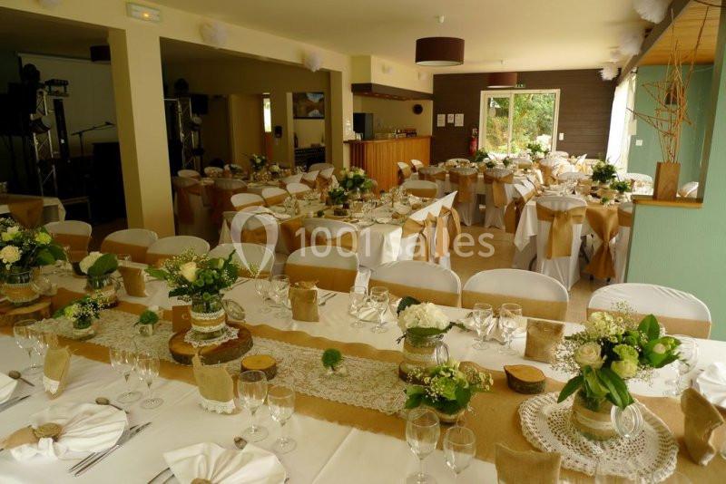 Salle de réception décorée avec des tables dressées, nappes blanches, chemins de table en jute et compositions florales.