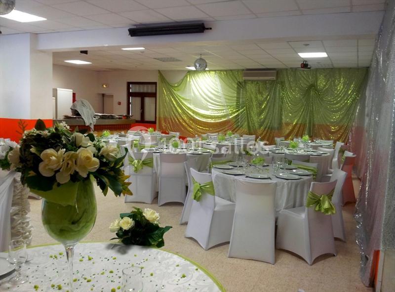 Salle de réception décorée avec des nappes blanches, des chaises ornées de rubans verts et des bouquets de fleurs.
