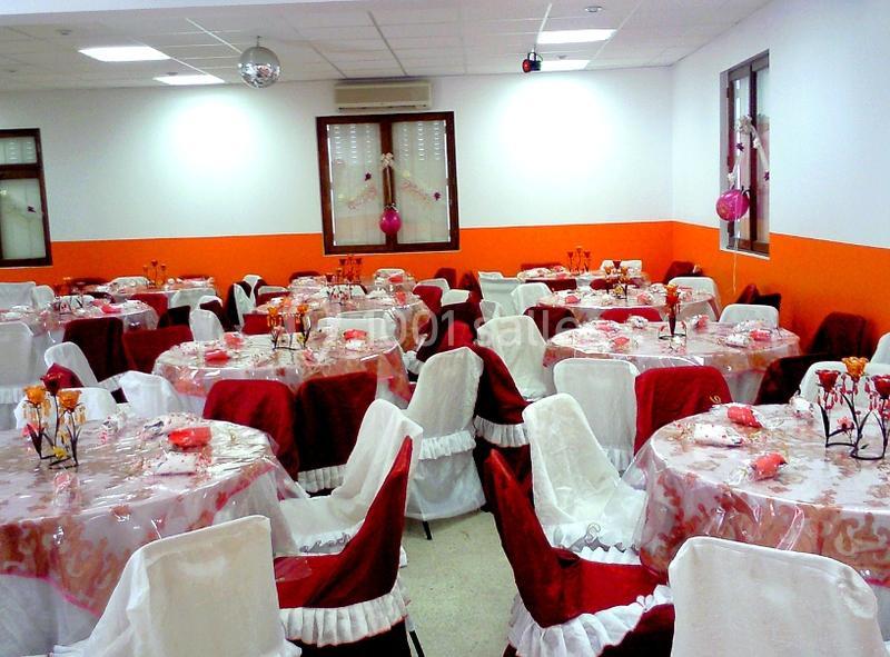 Salle décorée pour un événement avec des tables rondes recouvertes de nappes rouges et blanches, ornées de décorations.