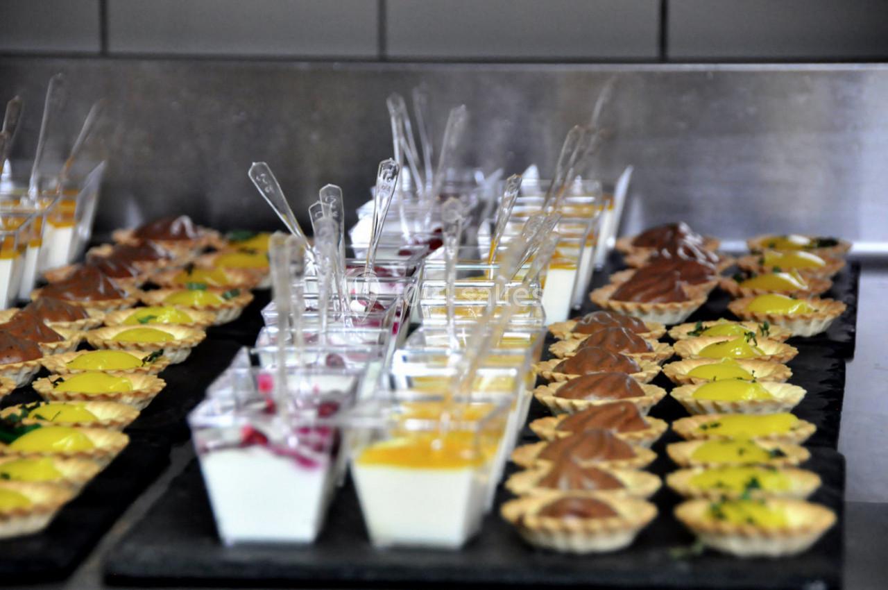 Assortiment de verrines et tartelettes sucrées disposées sur un plateau dans une cuisine professionnelle.