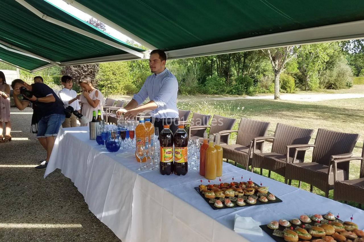 Un serveur prépare une table de buffet avec boissons et amuse-bouches sous un auvent en extérieur.