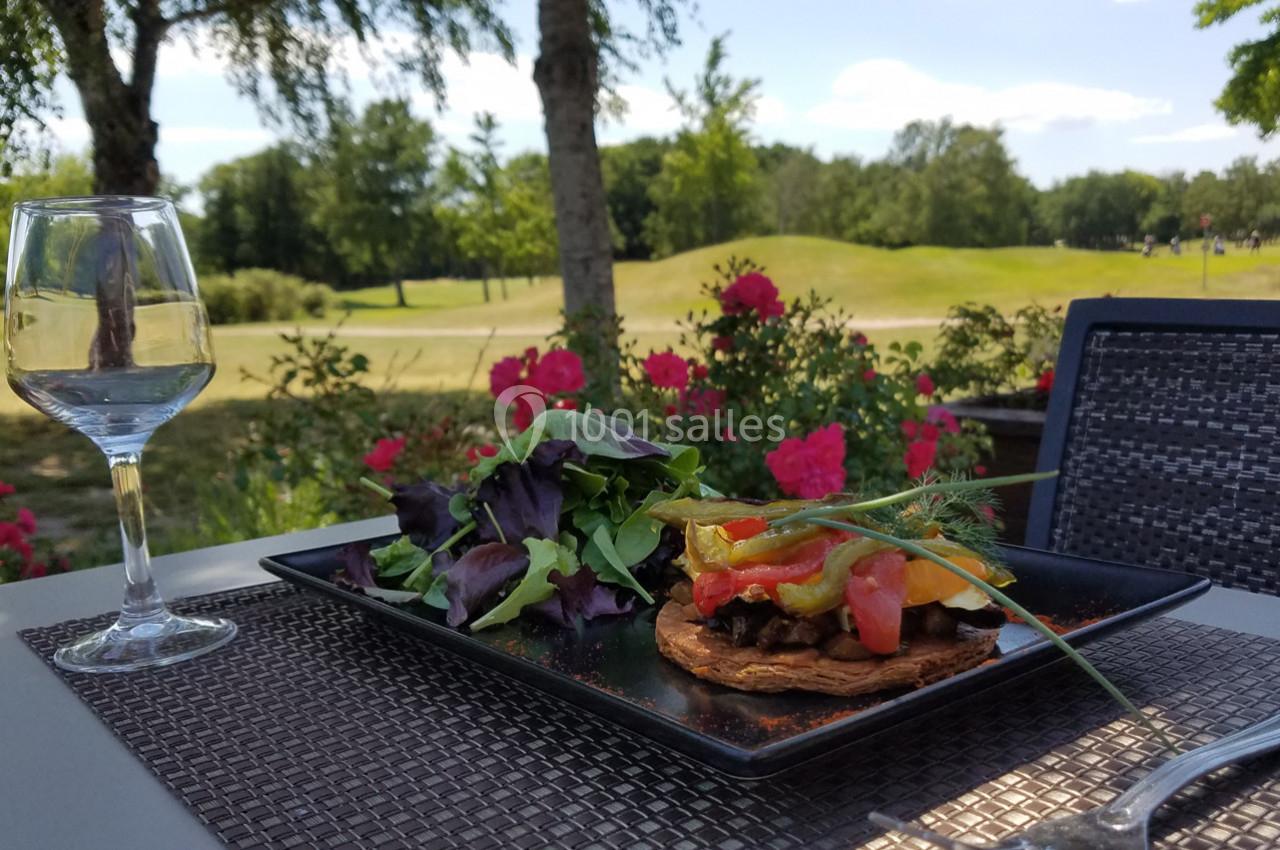 Assiette de légumes colorés sur une terrasse avec vue sur un jardin fleuri et un terrain de golf en arrière-plan.