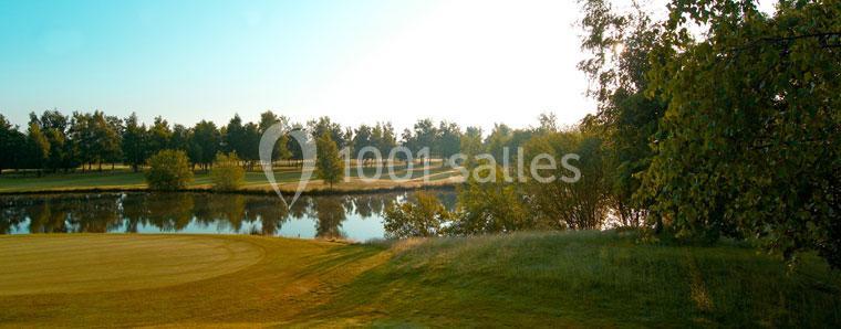 Paysage de golf avec un étang entouré d'arbres et une pelouse bien entretenue sous un ciel dégagé.