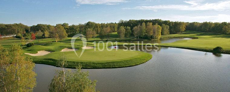 Vue d'un parcours de golf avec un green entouré d'eau, des bunkers de sable et des arbres en arrière-plan.