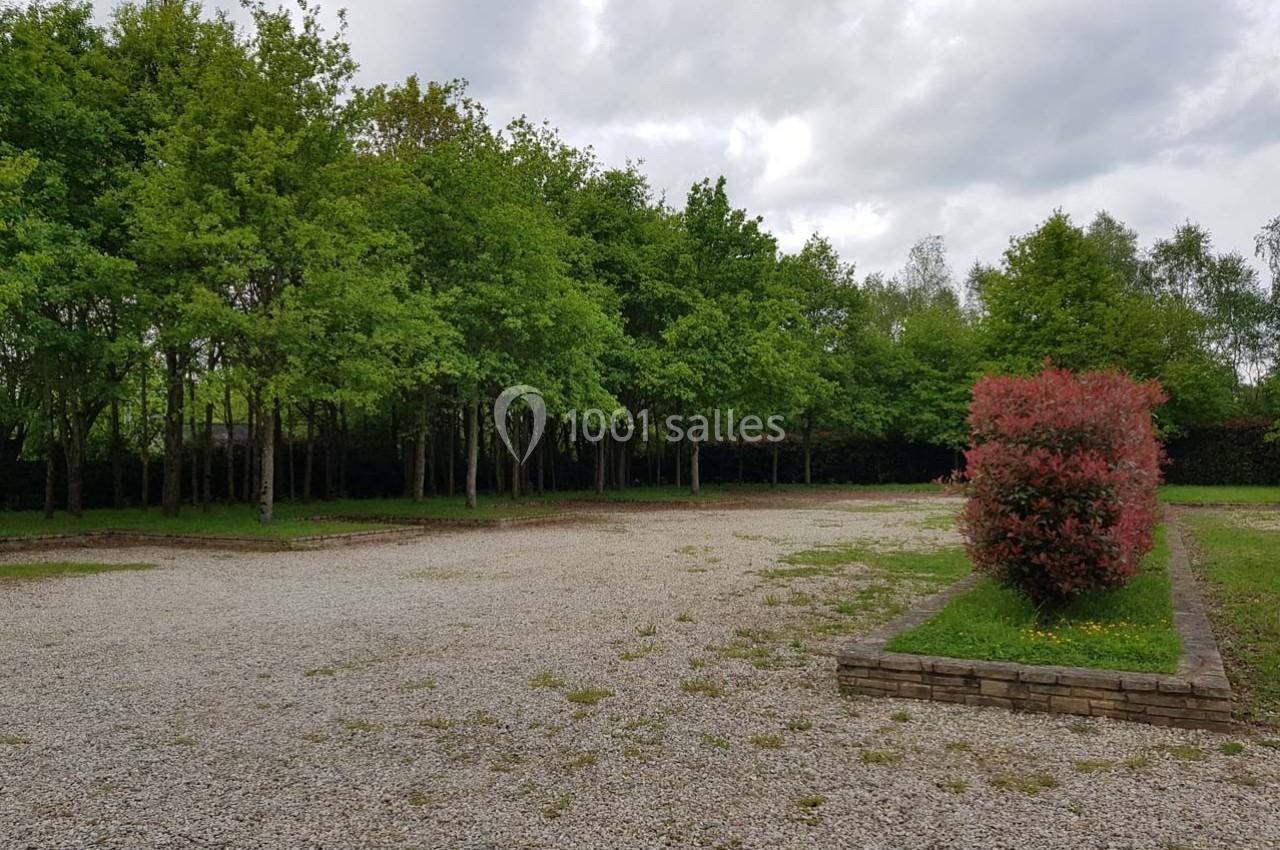 Parking en gravier entouré d'arbres et d'arbustes, avec un massif de plantes rouges au premier plan.