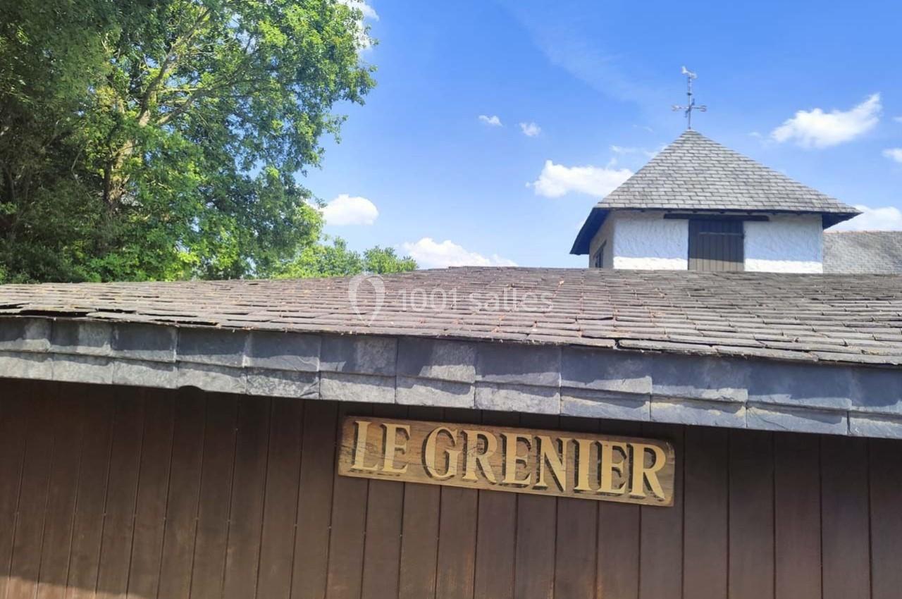 Façade en bois avec une enseigne ’Le Grenier’, sous un toit en ardoise, entourée de végétation et ciel bleu.