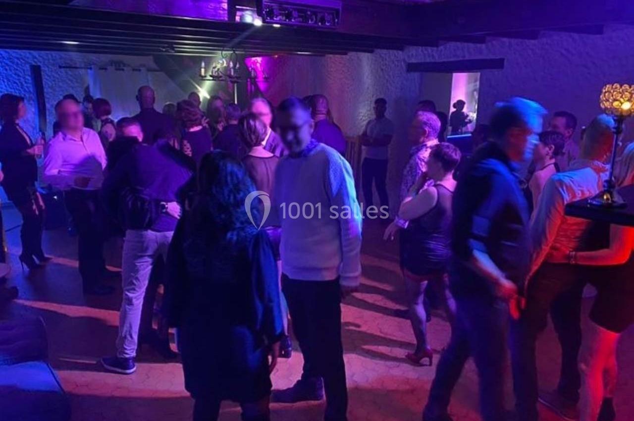 Des personnes dansent et discutent dans une salle éclairée par des lumières violettes et tamisées.