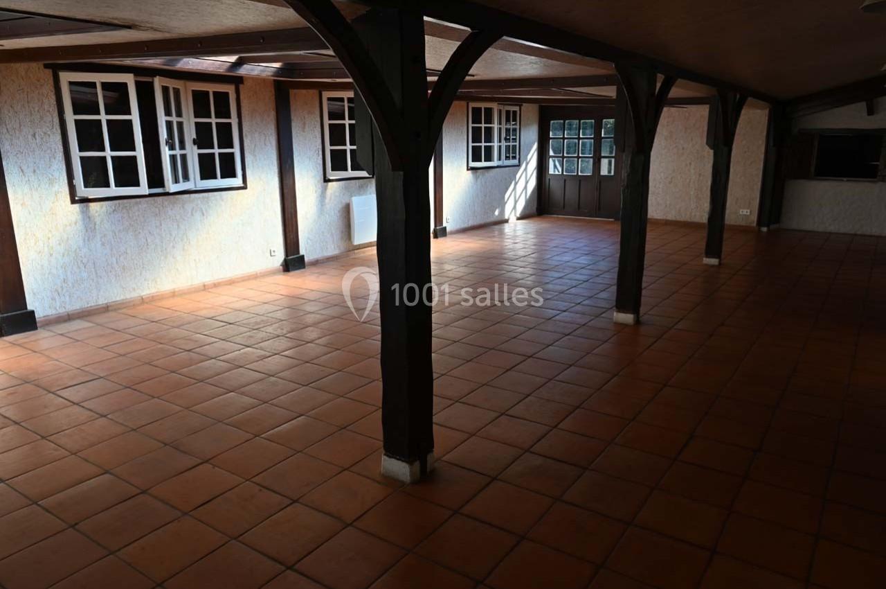 Salle spacieuse avec carrelage en terre cuite, poutres en bois et plusieurs fenêtres laissant entrer la lumière naturelle.