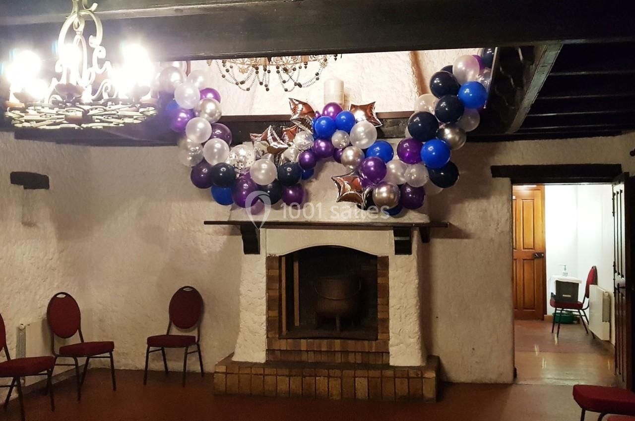 Cheminée décorée avec des ballons colorés et des étoiles argentées dans une salle avec des chaises et un lustre.