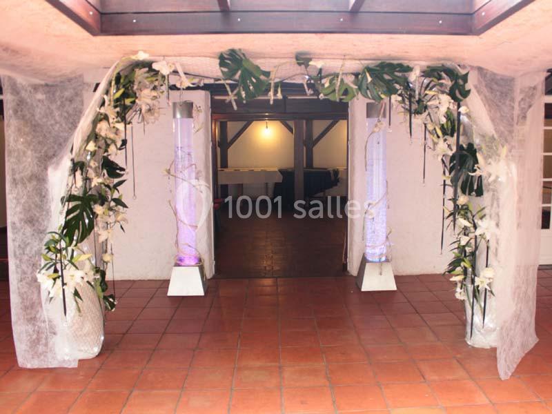 Entrée décorée avec des colonnes lumineuses, des fleurs blanches et des feuillages, sur un sol en carrelage rouge.