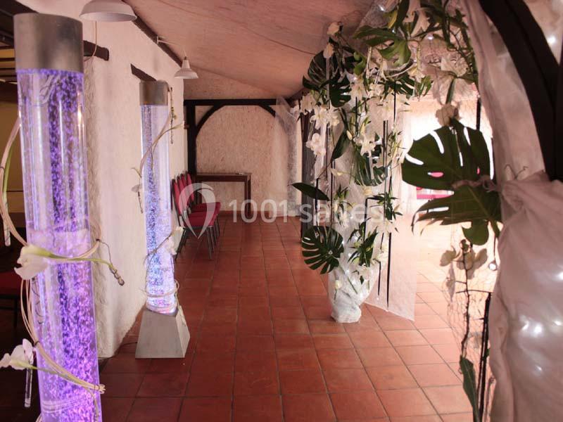 Allée décorée avec des colonnes lumineuses violettes, des plantes tropicales et des fleurs blanches dans une salle carrelée.
