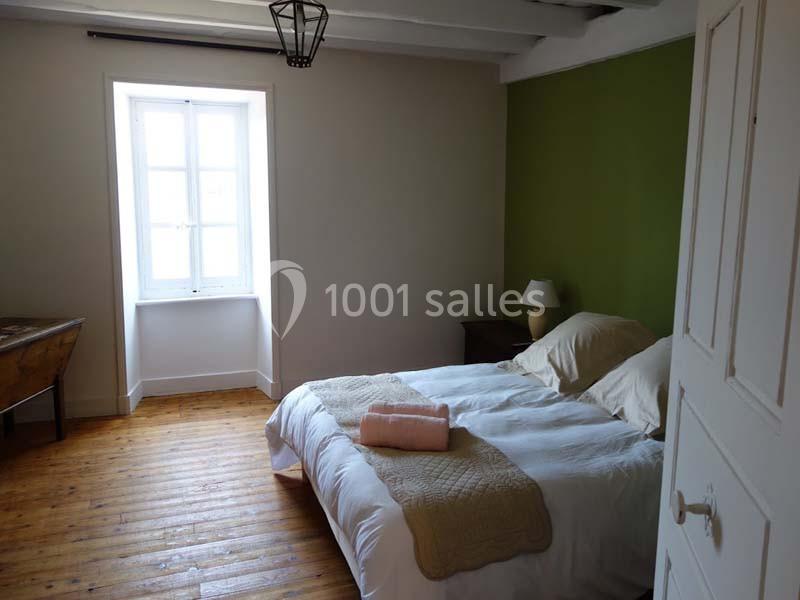 Chambre lumineuse avec lit double, mur vert, parquet en bois et fenêtre laissant entrer la lumière naturelle.