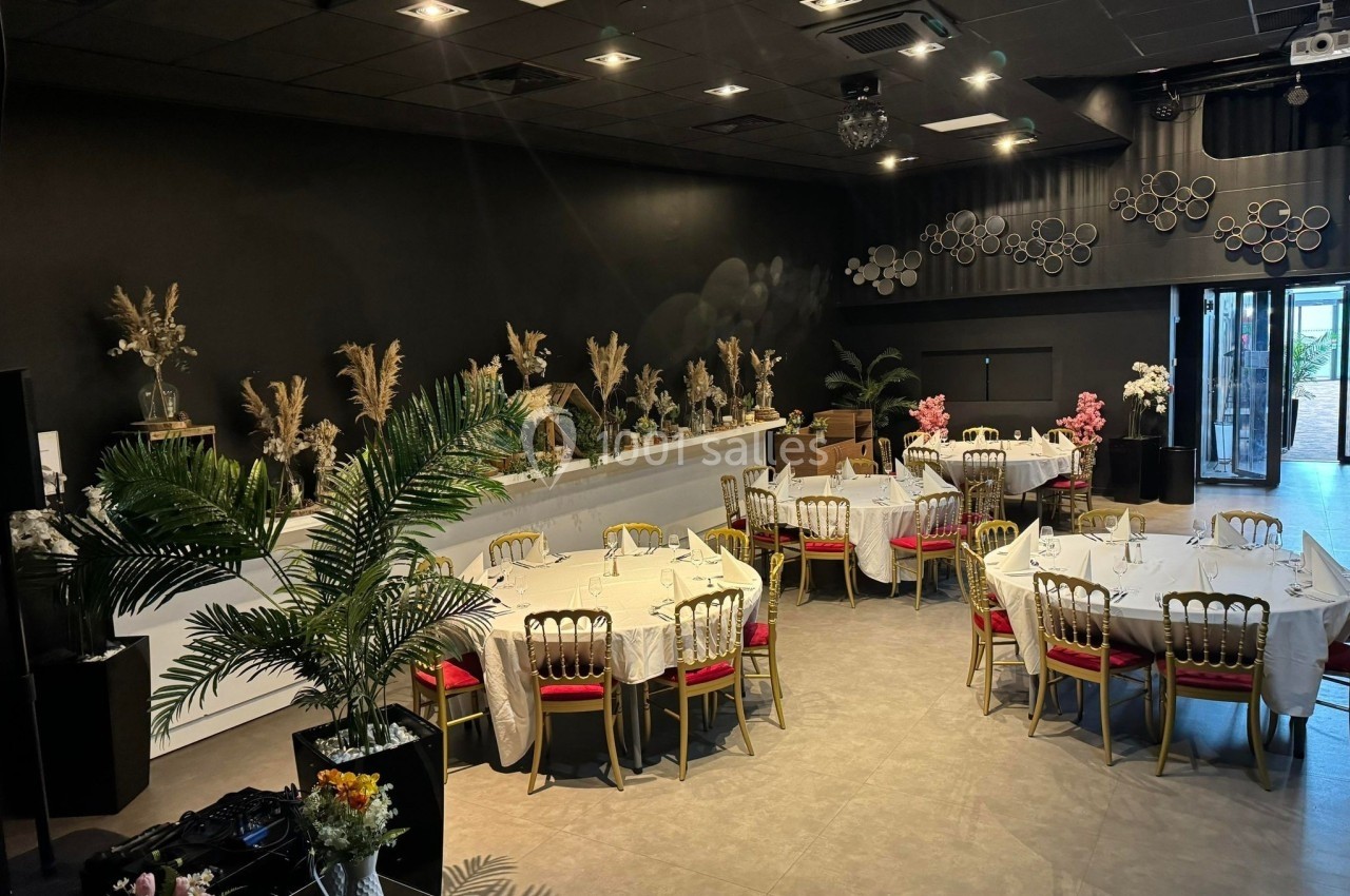 Salle de réception élégante avec tables rondes dressées, décorations florales et lumière naturelle entrant par une baie…
