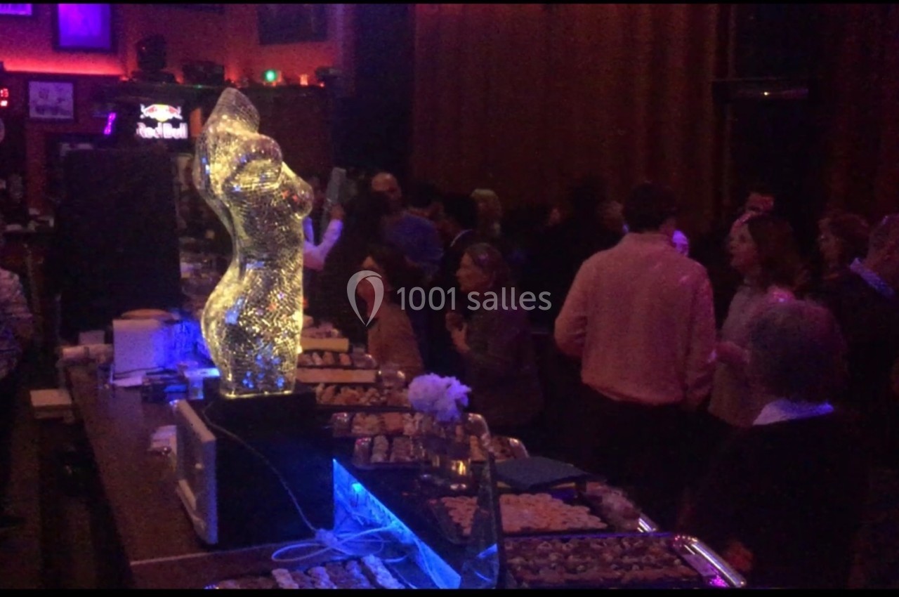 Personnes rassemblées dans un lieu sombre avec un buffet éclairé et une sculpture lumineuse en premier plan.