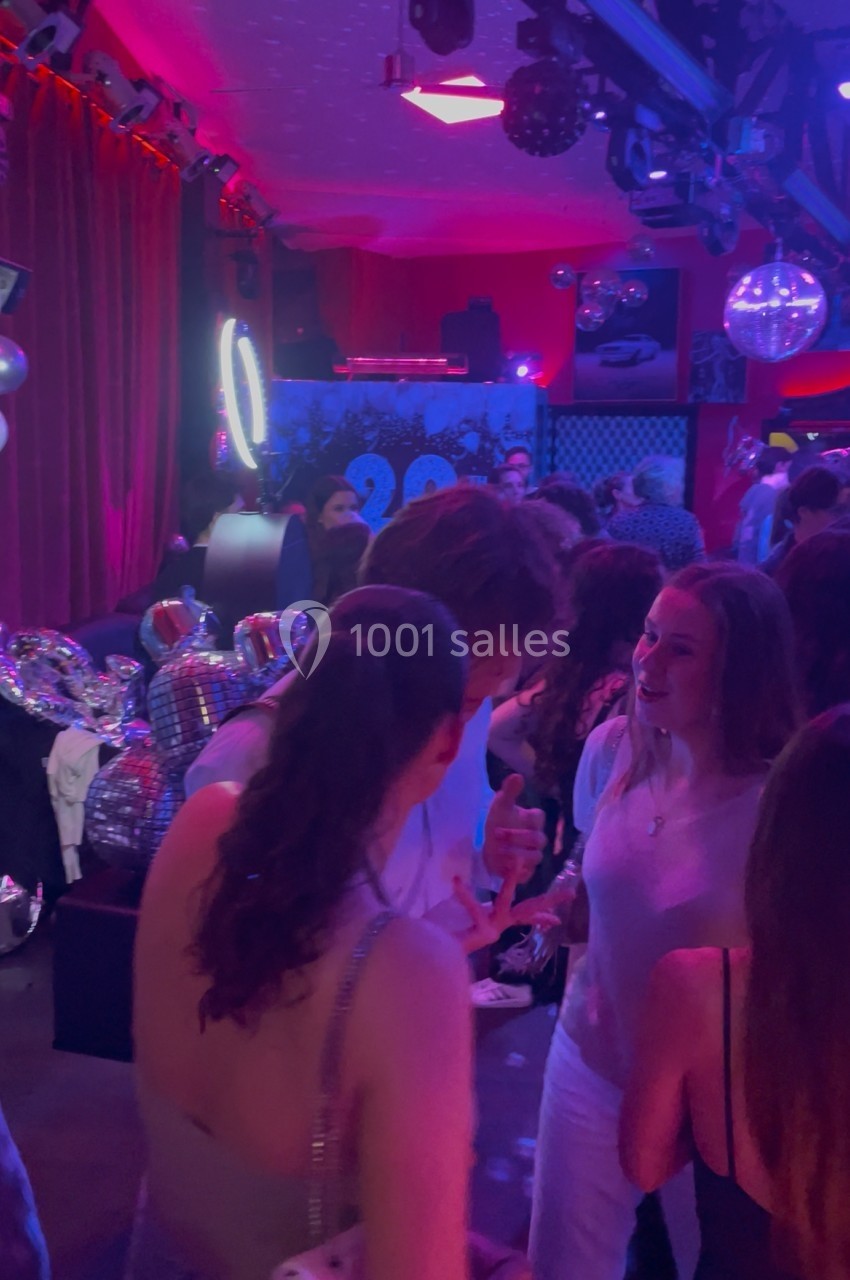 Des personnes discutent et dansent dans une ambiance festive avec éclairage coloré et boules à facettes.