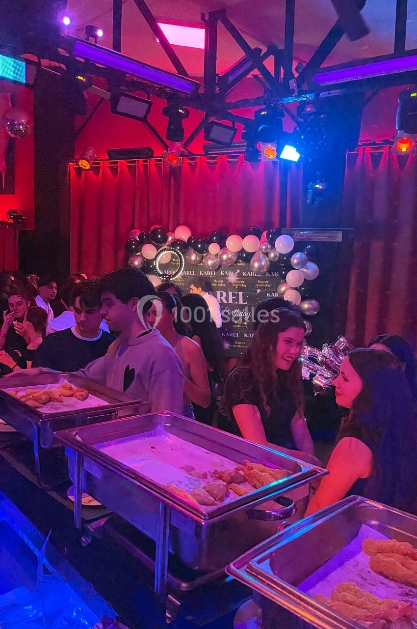 Des personnes se servent à un buffet dans une salle décorée avec des ballons et un éclairage coloré.