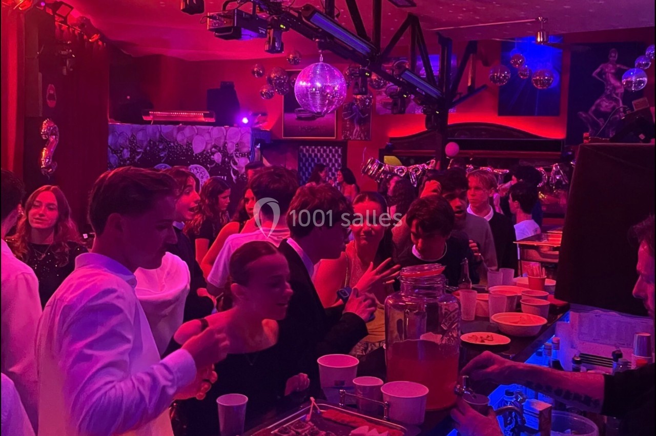 Des jeunes discutent et se servent à un buffet dans une ambiance festive avec éclairage coloré et décorations.