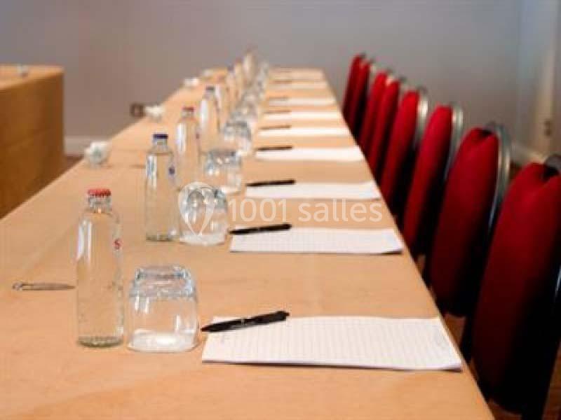 Salle de réunion avec une longue table dressée, comprenant des blocs-notes, des stylos et des bouteilles d'eau.