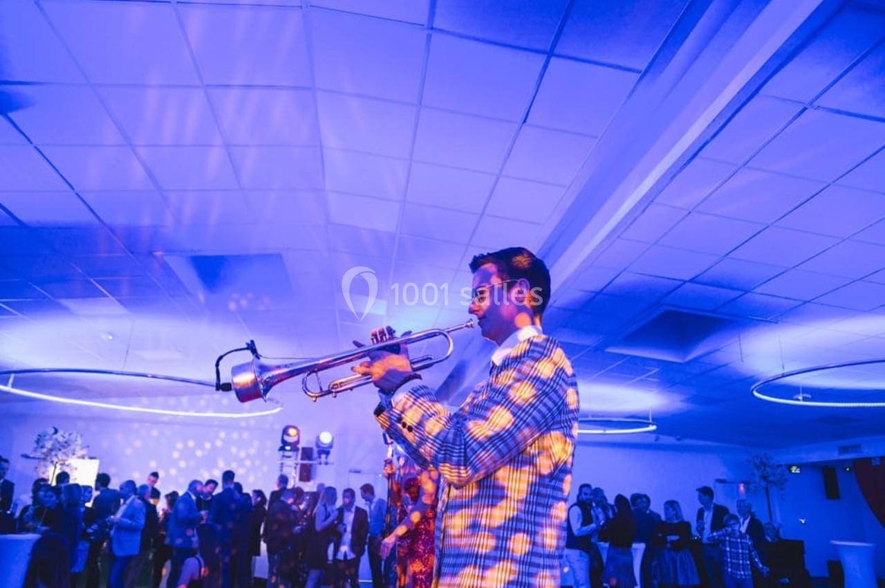 Un musicien joue de la trompette dans une salle éclairée par des lumières bleues, avec un public en arrière-plan.