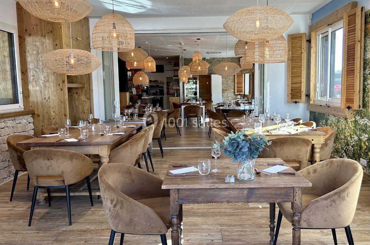 Salle de restaurant lumineuse avec tables en bois, chaises en velours beige et suspensions en osier.