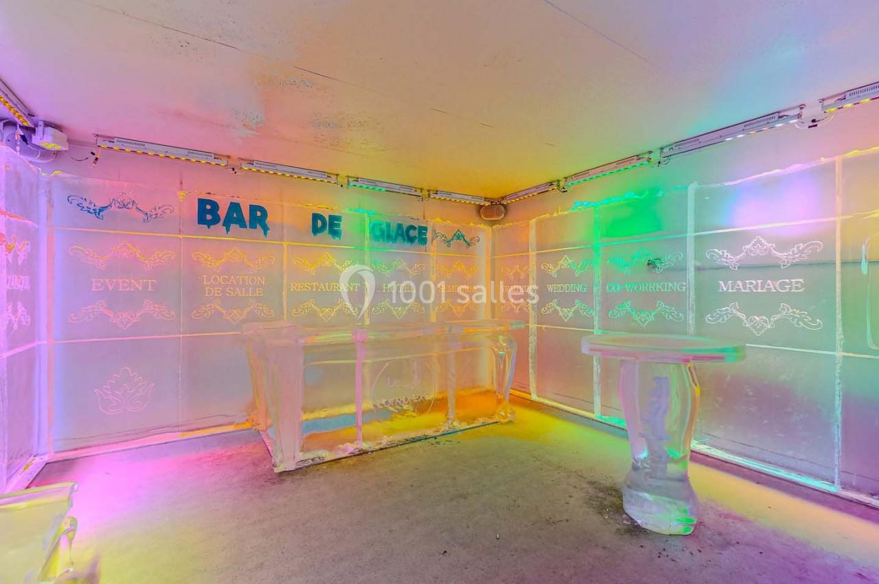 Salle en glace avec des murs gravés de textes colorés et un comptoir, éclairée par des lumières multicolores.