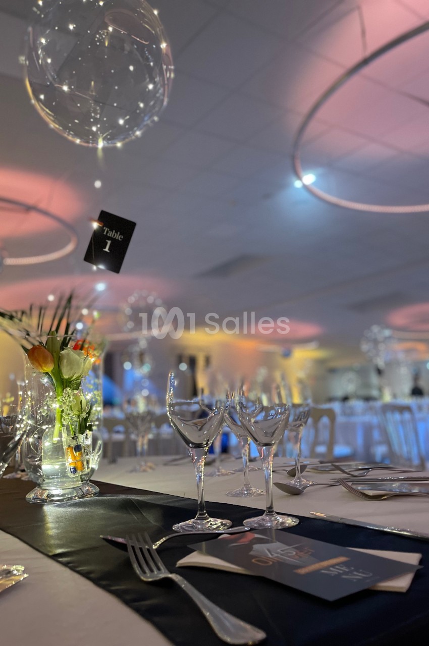 Table élégamment dressée avec des verres, des couverts, un centre de table floral et une ambiance lumineuse tamisée.