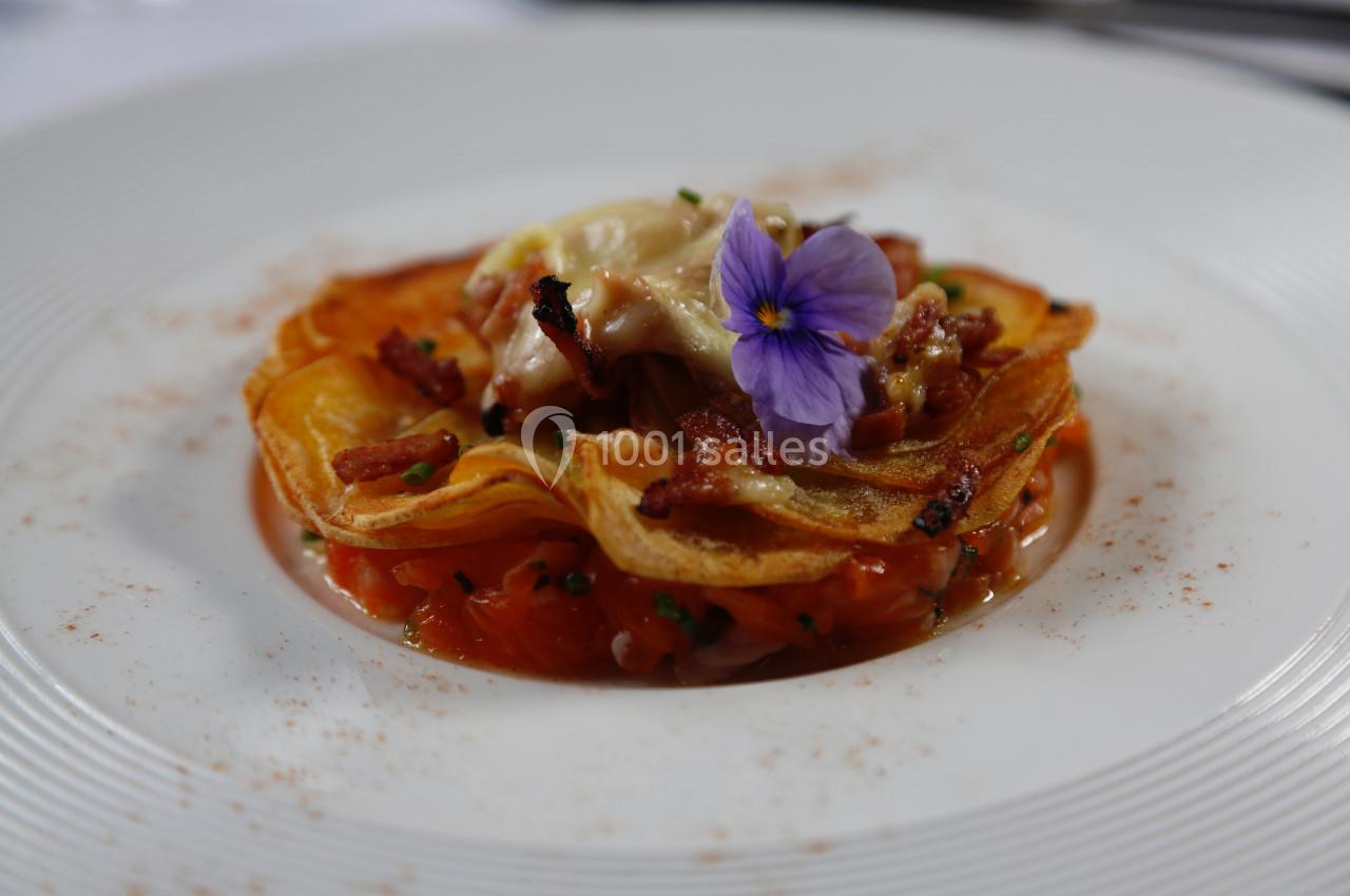 Assiette garnie d'une fine galette croustillante, saumon, lardons et fleur comestible en décoration.