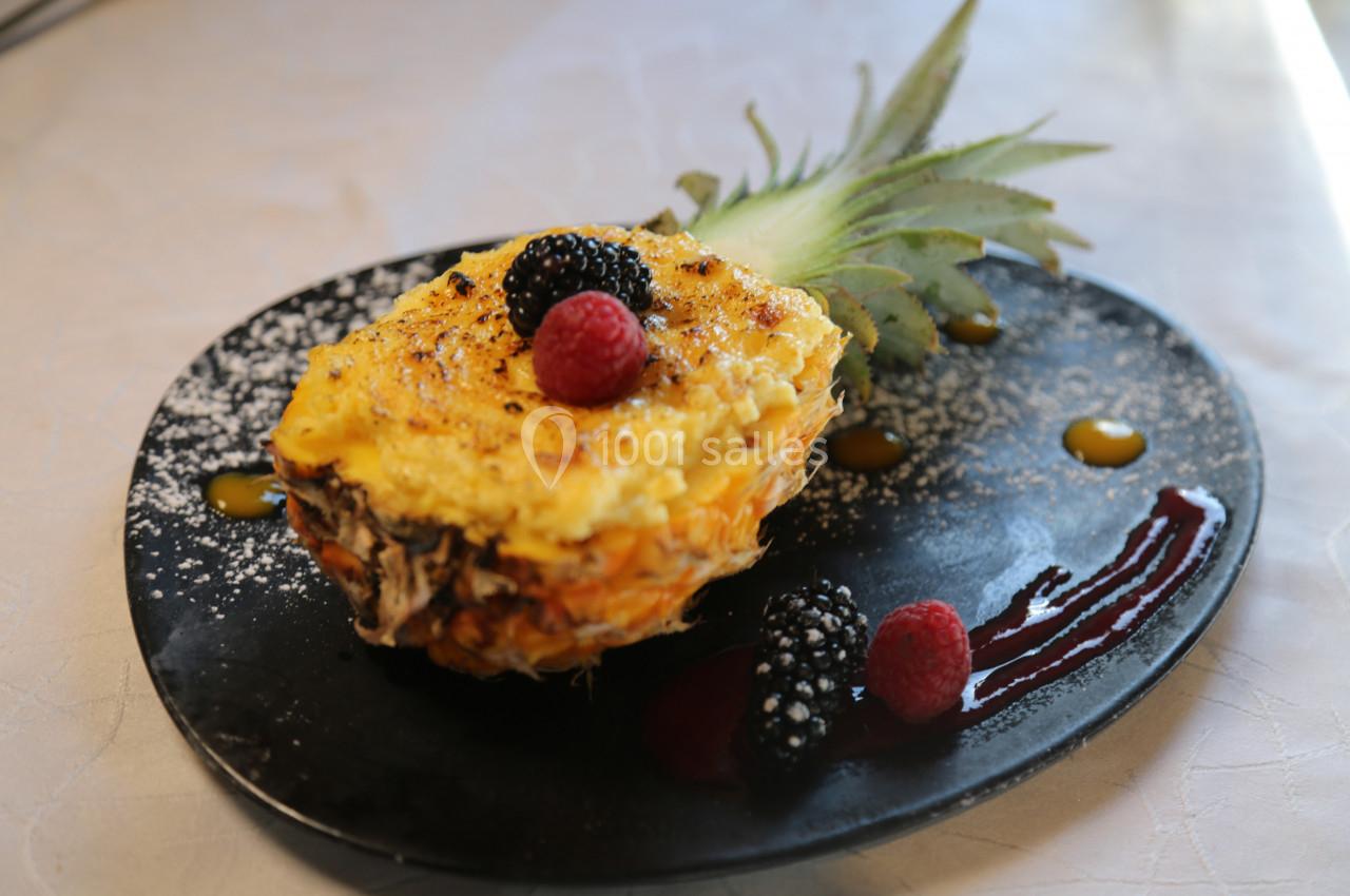 Demi-ananas garni d'un gratin sucré, décoré de fruits rouges et de coulis, présenté sur une assiette noire.