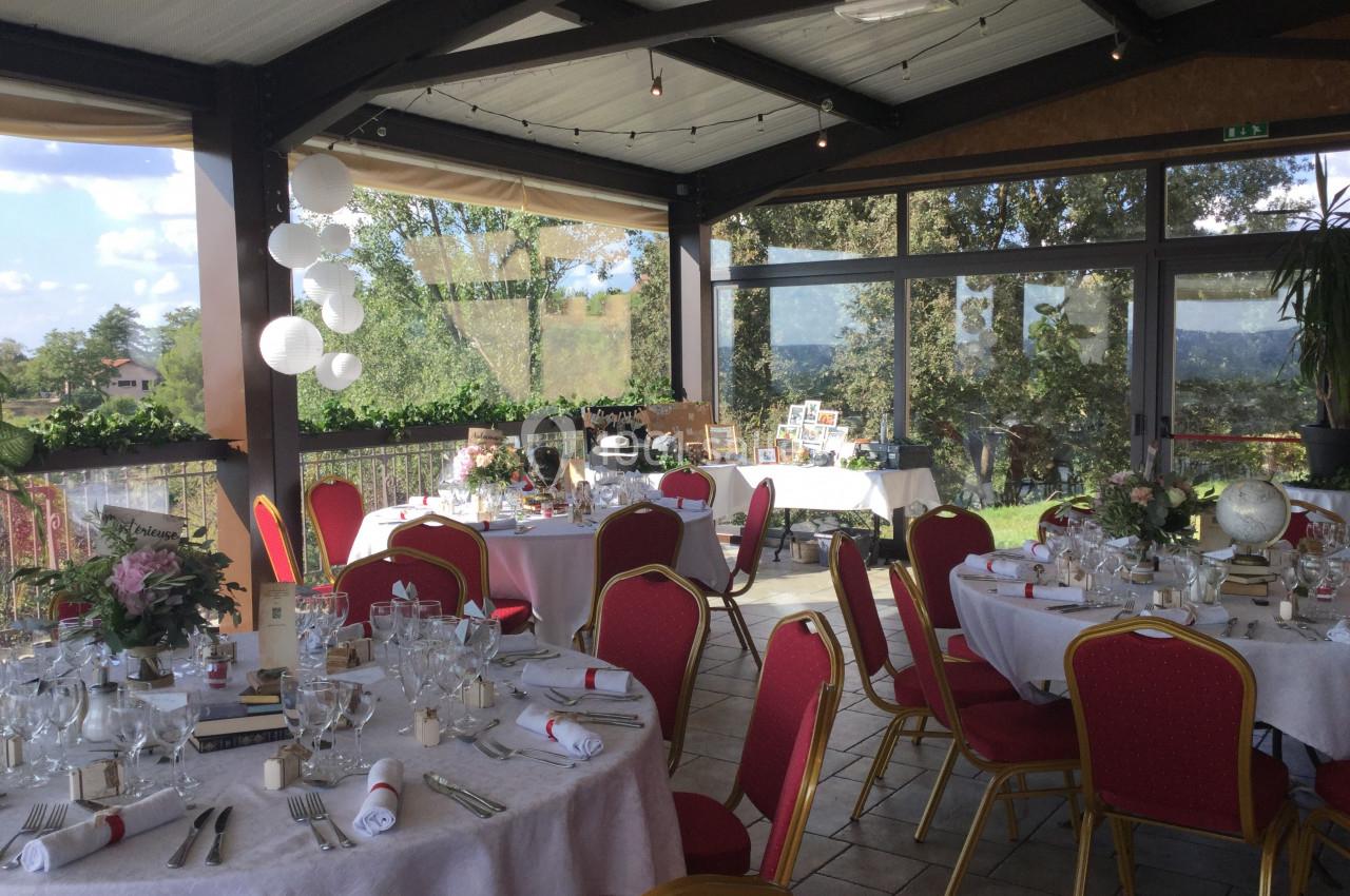 Salle de réception lumineuse avec tables décorées pour un événement, entourée de grandes baies vitrées donnant sur un…