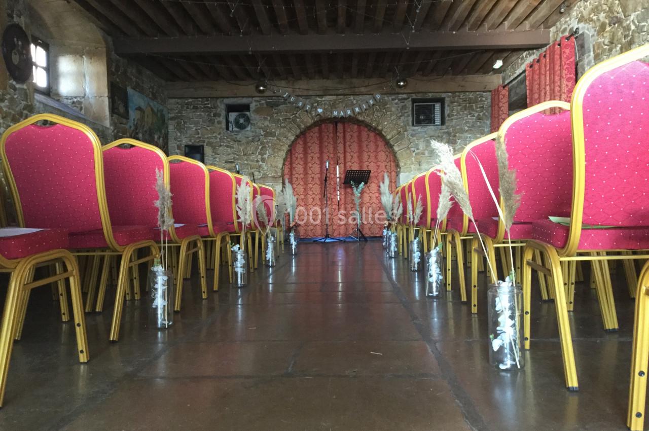 Rangées de chaises rouges alignées dans une salle en pierre avec poutres apparentes, décorée pour un événement.