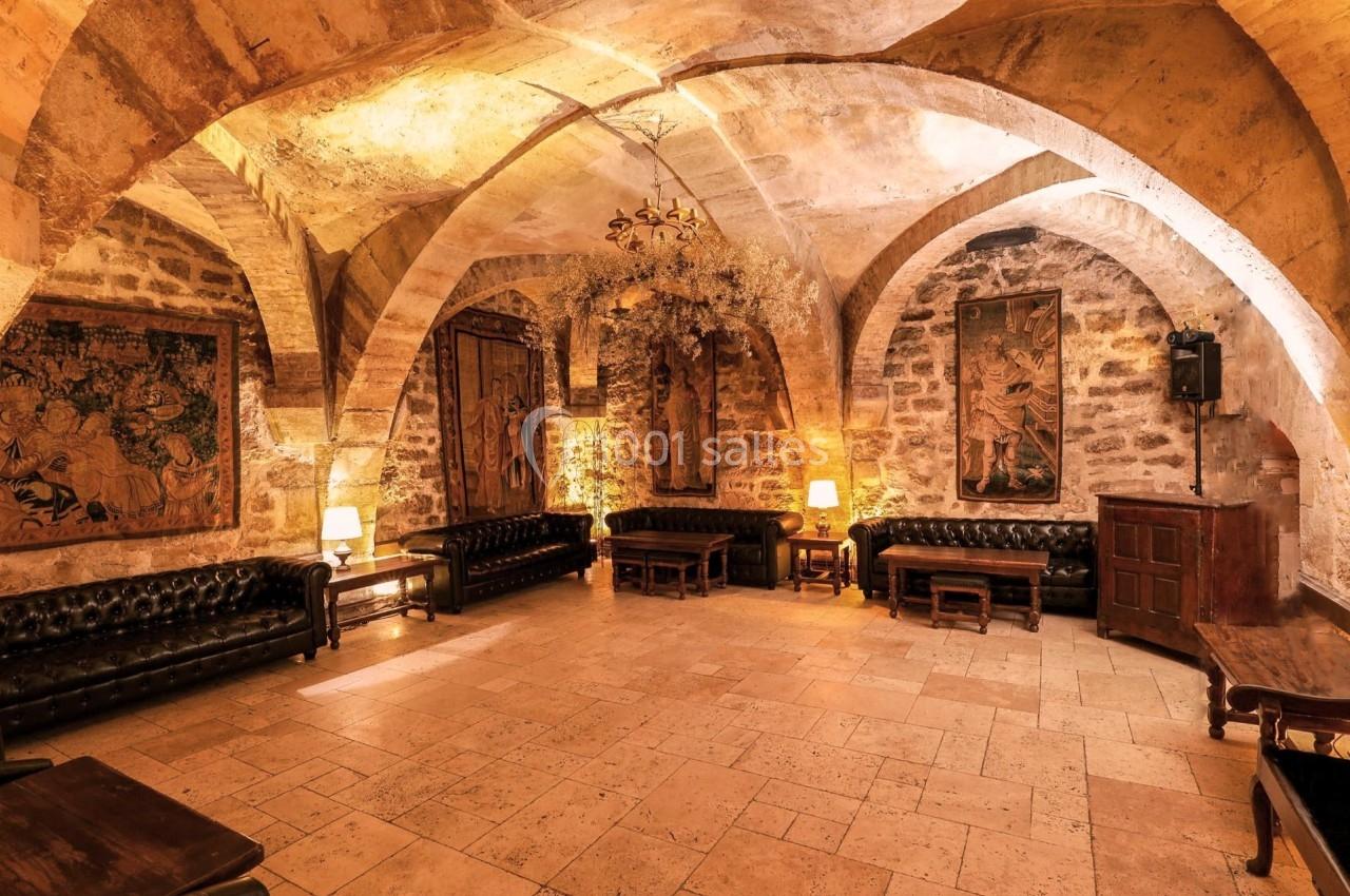 Salle voûtée en pierre avec canapés en cuir, tapisseries murales, éclairage chaleureux et mobilier en bois.