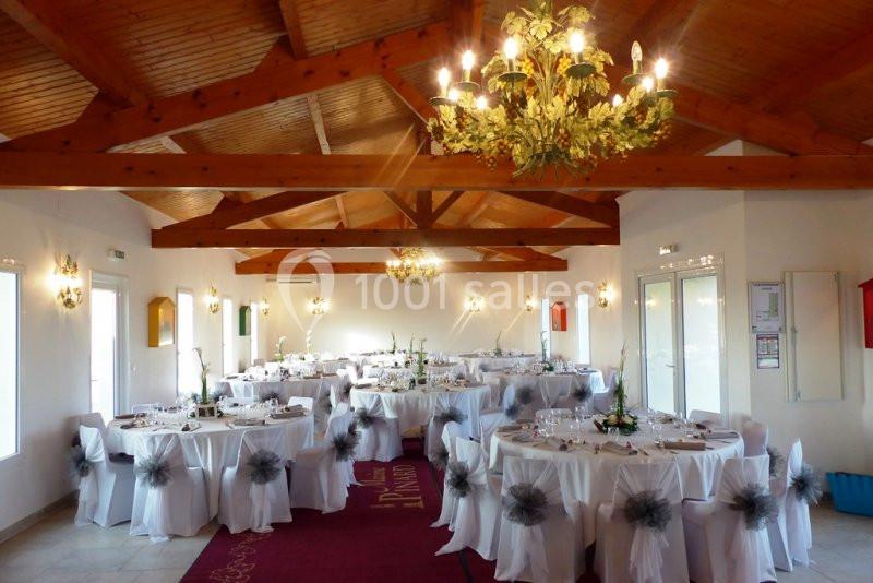 Salle de réception lumineuse avec tables rondes dressées, nappes blanches et décoration florale, sous un plafond en bois.
