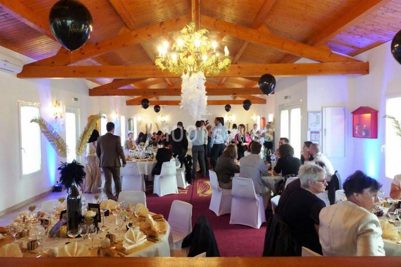 Salle de réception décorée, avec des invités assis à des tables dressées et d'autres debout discutant.