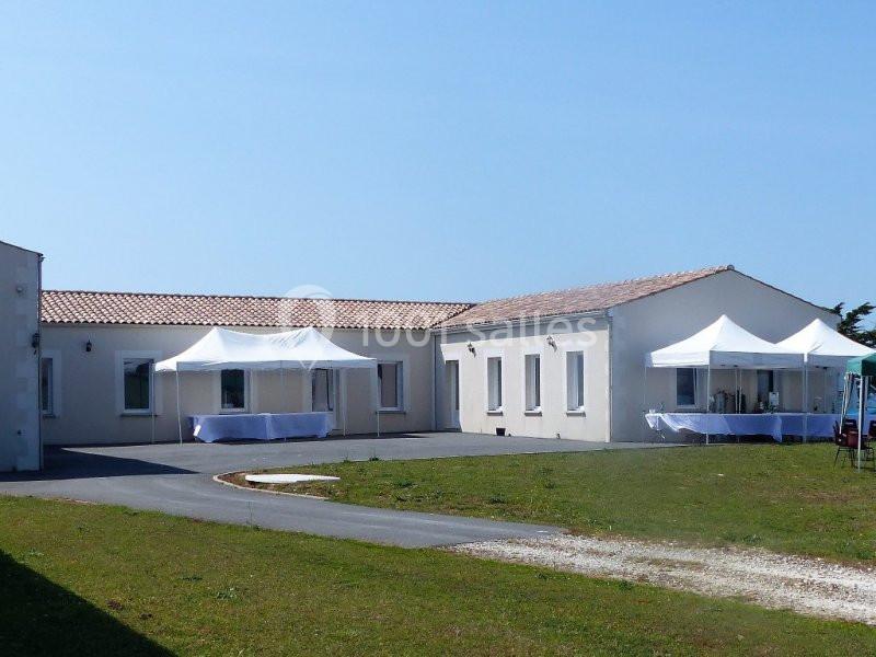 Bâtiment clair de plain-pied avec des tentes blanches installées à l'extérieur sur une pelouse et une allée goudronnée.