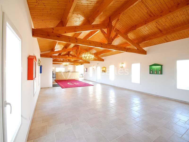 Salle lumineuse avec plafond en bois, sol carrelé clair, grandes fenêtres et comptoir au fond.