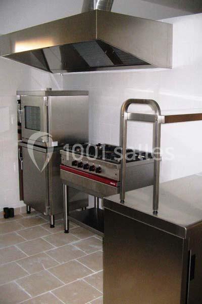 Cuisine professionnelle avec four, plaque de cuisson, hotte en inox et mobilier en acier inoxydable sur sol carrelé.