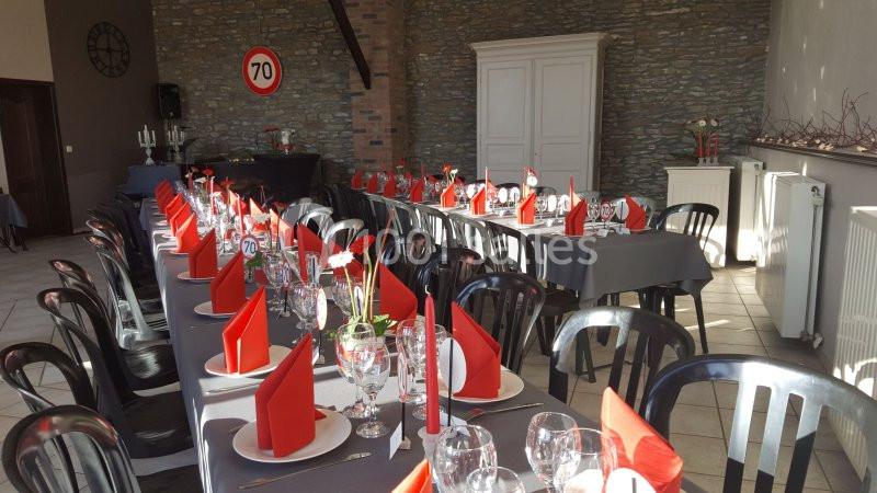 Salle de réception avec tables dressées, nappes grises, serviettes rouges pliées et décorations florales.