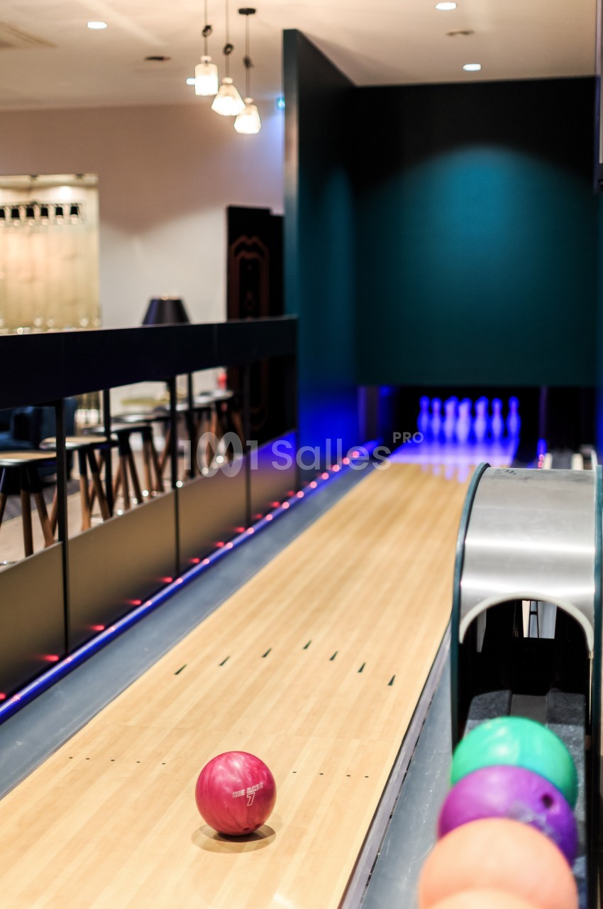 Piste de bowling avec une boule rouge en mouvement et des quilles alignées au fond, éclairage tamisé.