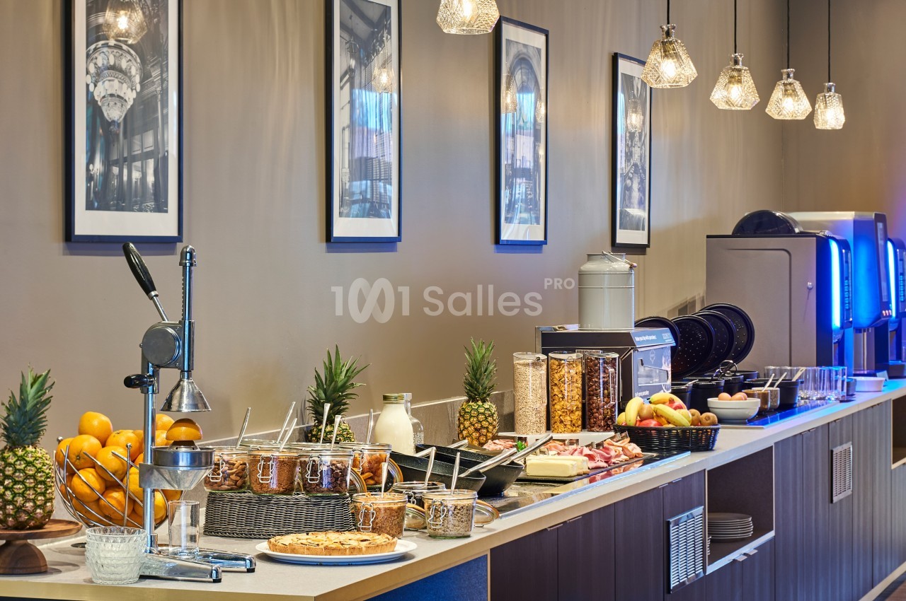 Buffet de petit-déjeuner avec fruits frais, viennoiseries, céréales, jus et machine à boissons dans un cadre lumineux.