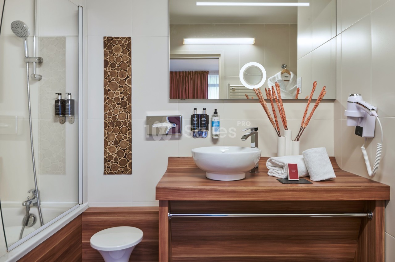 Salle de bain moderne avec lavabo sur meuble en bois, miroir, douche, sèche-cheveux et accessoires de toilette.