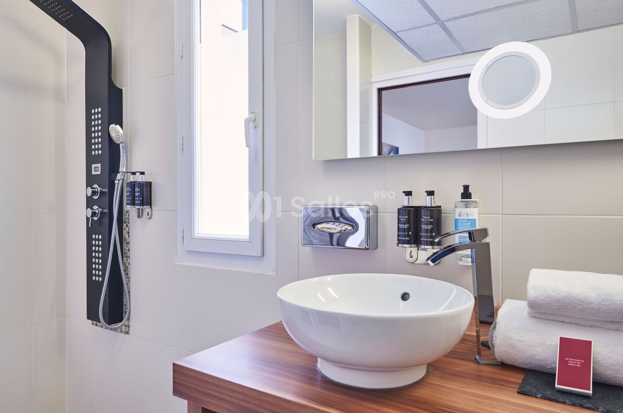 Salle de bain moderne avec lavabo sur meuble en bois, miroir éclairé, douche à jets et serviettes pliées.
