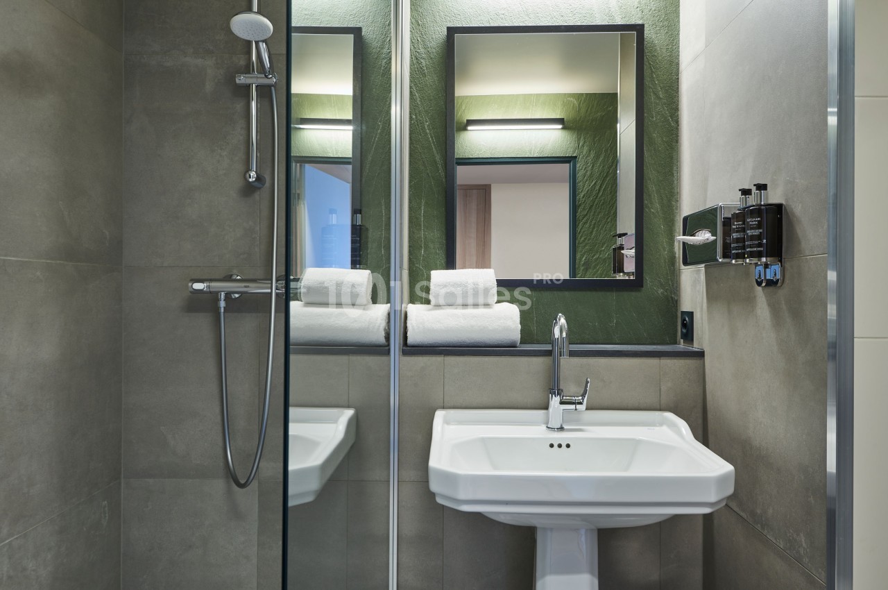 Salle de bain moderne avec douche, lavabo blanc, miroir encadré et serviettes pliées sur une étagère.
