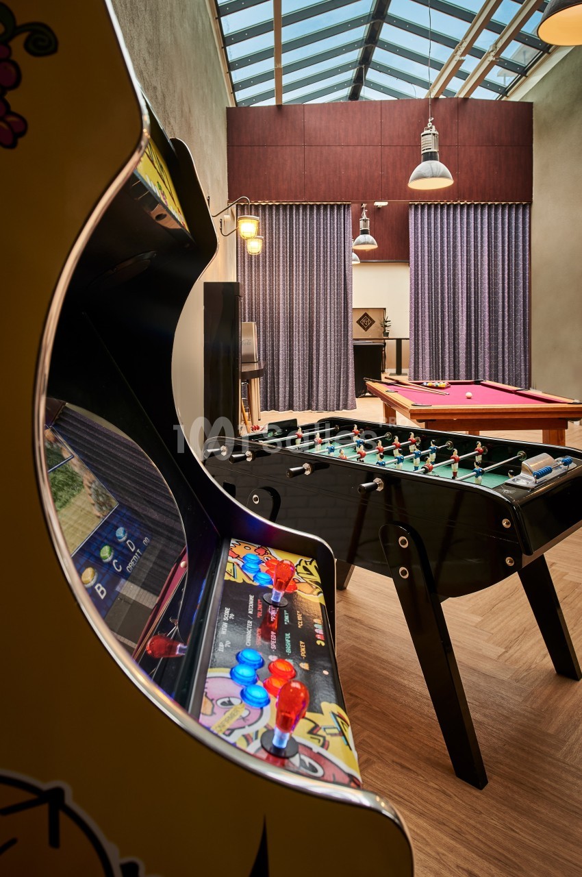 Salle de jeux avec une borne d'arcade, un baby-foot et une table de billard sous un toit en verre.
