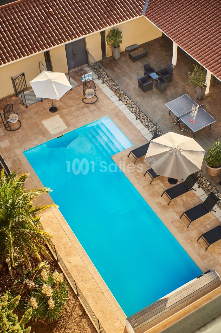 Vue aérienne d'une piscine extérieure entourée de chaises longues, parasols et mobilier de jardin sur une terrasse…