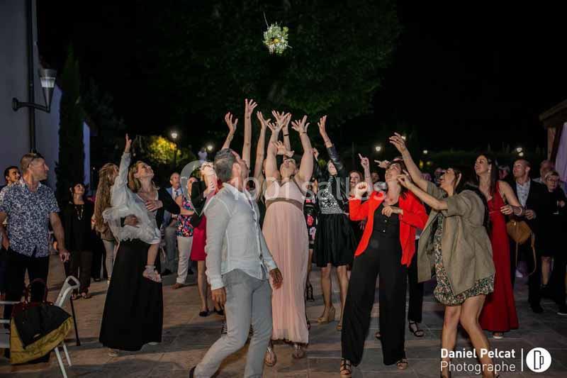 Un groupe de personnes tend les bras pour attraper un bouquet lancé lors d'une fête en extérieur, de nuit.
