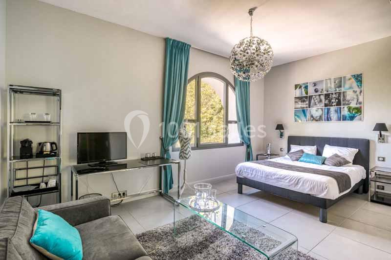 Chambre lumineuse avec lit double, canapé, télévision, rideaux turquoise et décoration moderne.