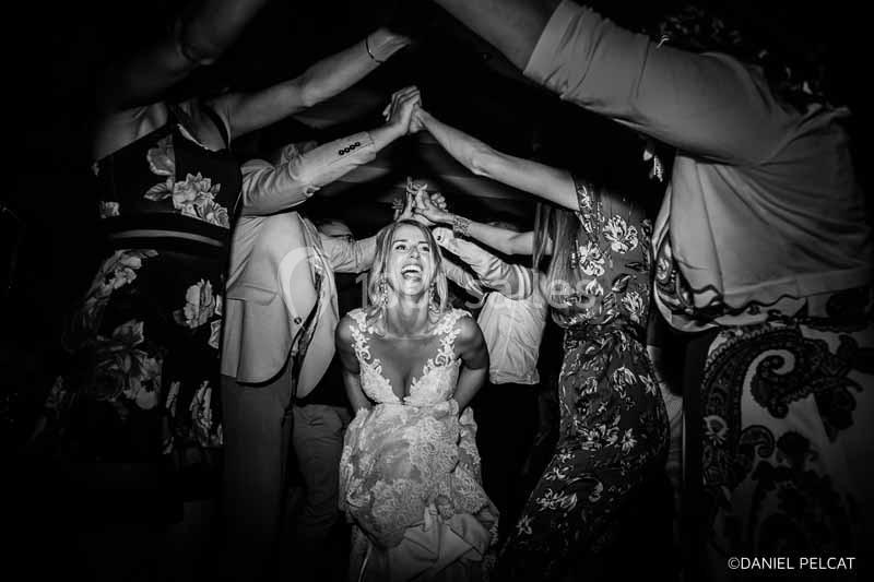 Une mariée souriante passe sous une arche formée par les bras levés des invités lors d'une fête.