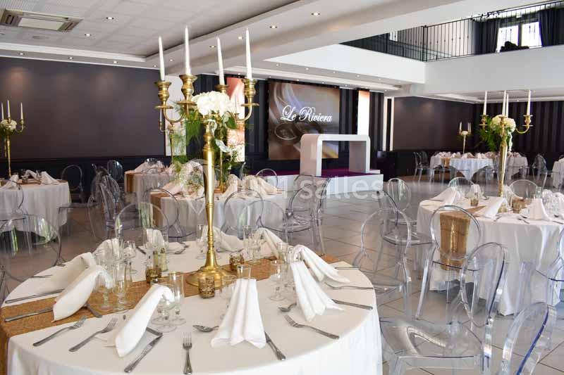 Salle de réception élégante avec tables rondes dressées, chaises transparentes et chandeliers dorés décorés de fleurs…